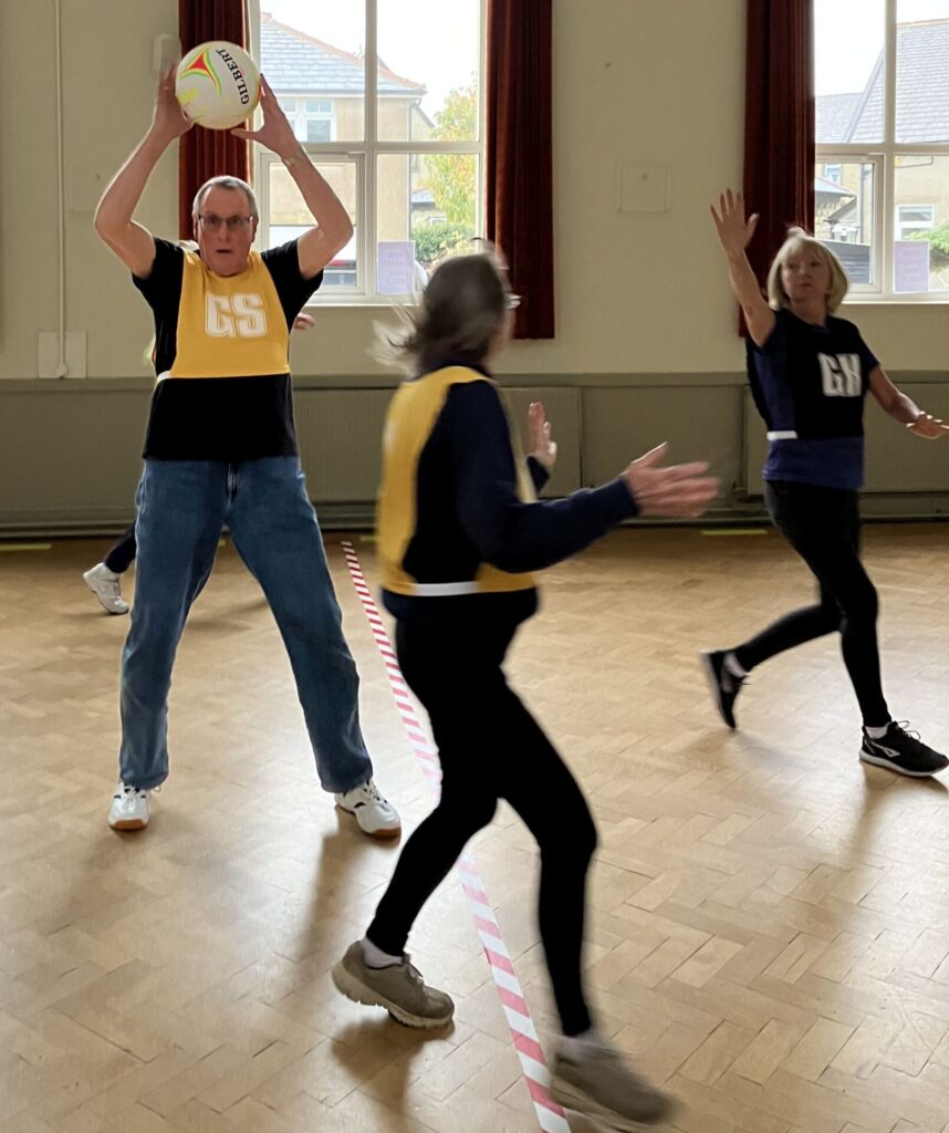 An action shot of people playing walking netball. There are two women in the picture and one man.