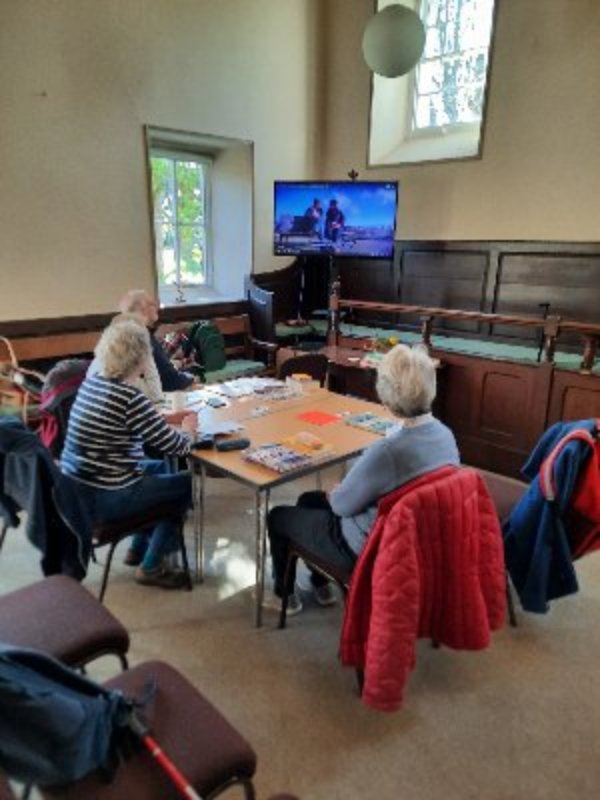 A Spanish conversation class in the Quaker Meeting House in Settle. Several people are sitting at a table looking at a screen.